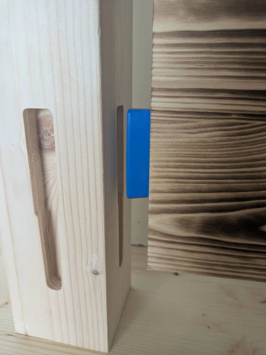 Clip bleu engagé sur le chant d'un panneau, contre une façade en bois brûlé