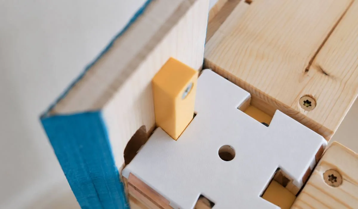 Connecteur blanc et cale jaune vissés à l'angle d'un panneau à chant bleu